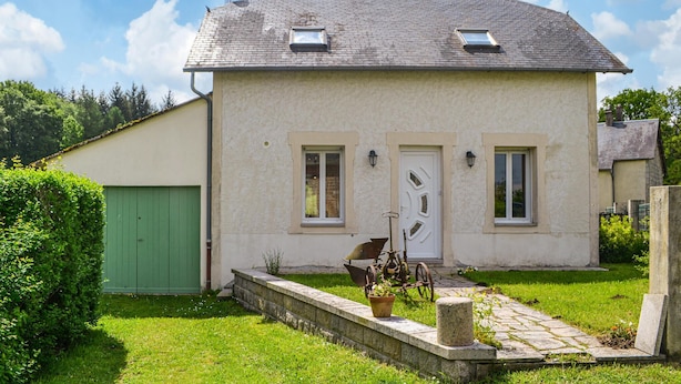 Une maison à deux étages avec une porte verte, deux fenêtres et un petit porche agrémenté d’un pot de fleurs.