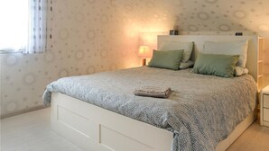 Un lit bien fait, recouvert d’une couvre-lit à motifs, avec une lampe de chevet et deux oreillers posés sur une tête de lit blanche.