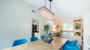 A modern dining area with a wooden table and blue chairs, a chandelier, and a plant centerpiece. - Mid-century Modern Villa w/ Pool Near Universal (Orlando)