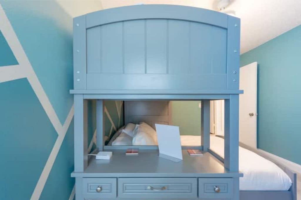 Un lit superposé avec un bureau en dessous, des tiroirs et une petite fenêtre.