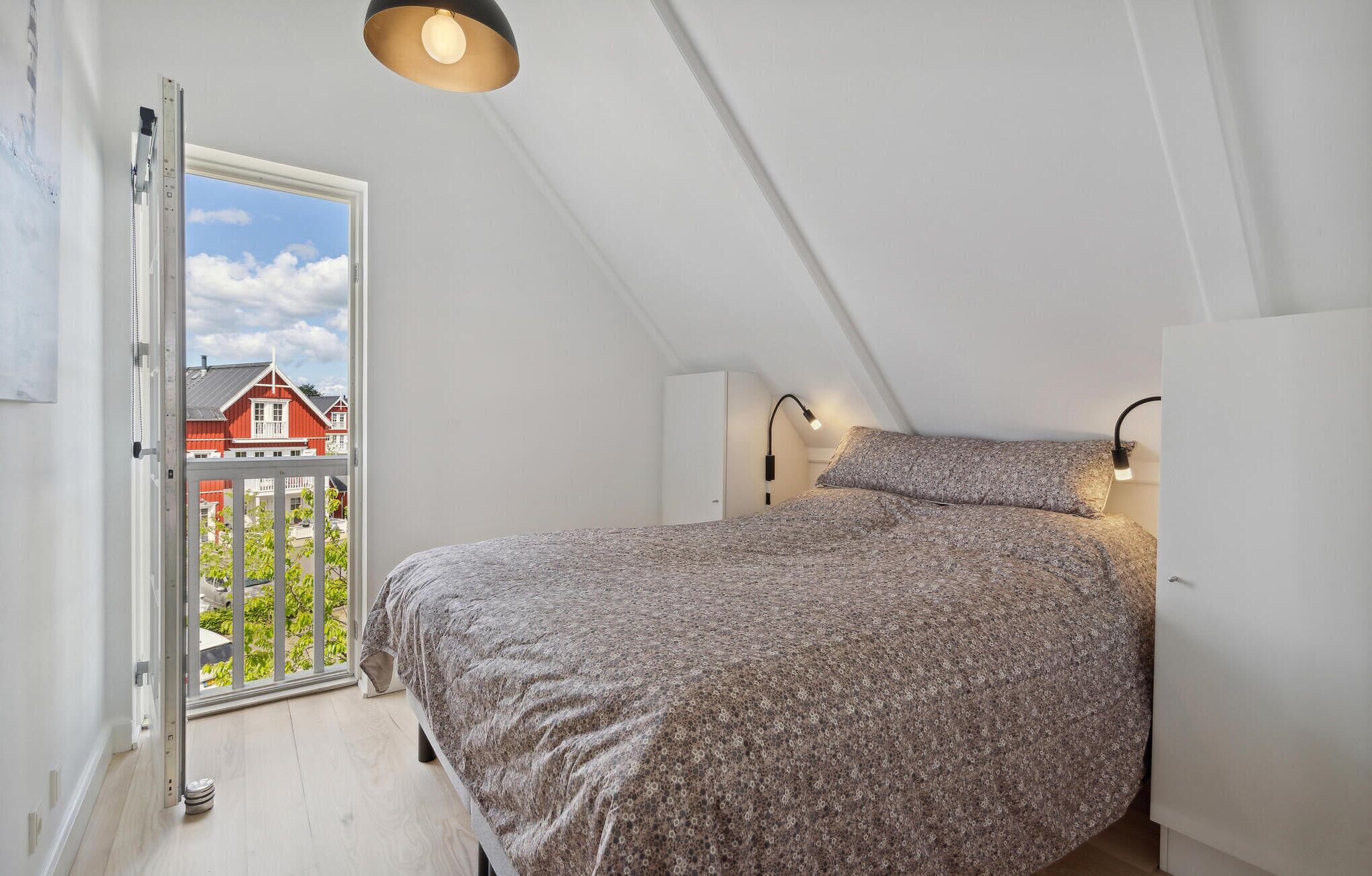 A bedroom with a bed, a window, and a view of a red house.