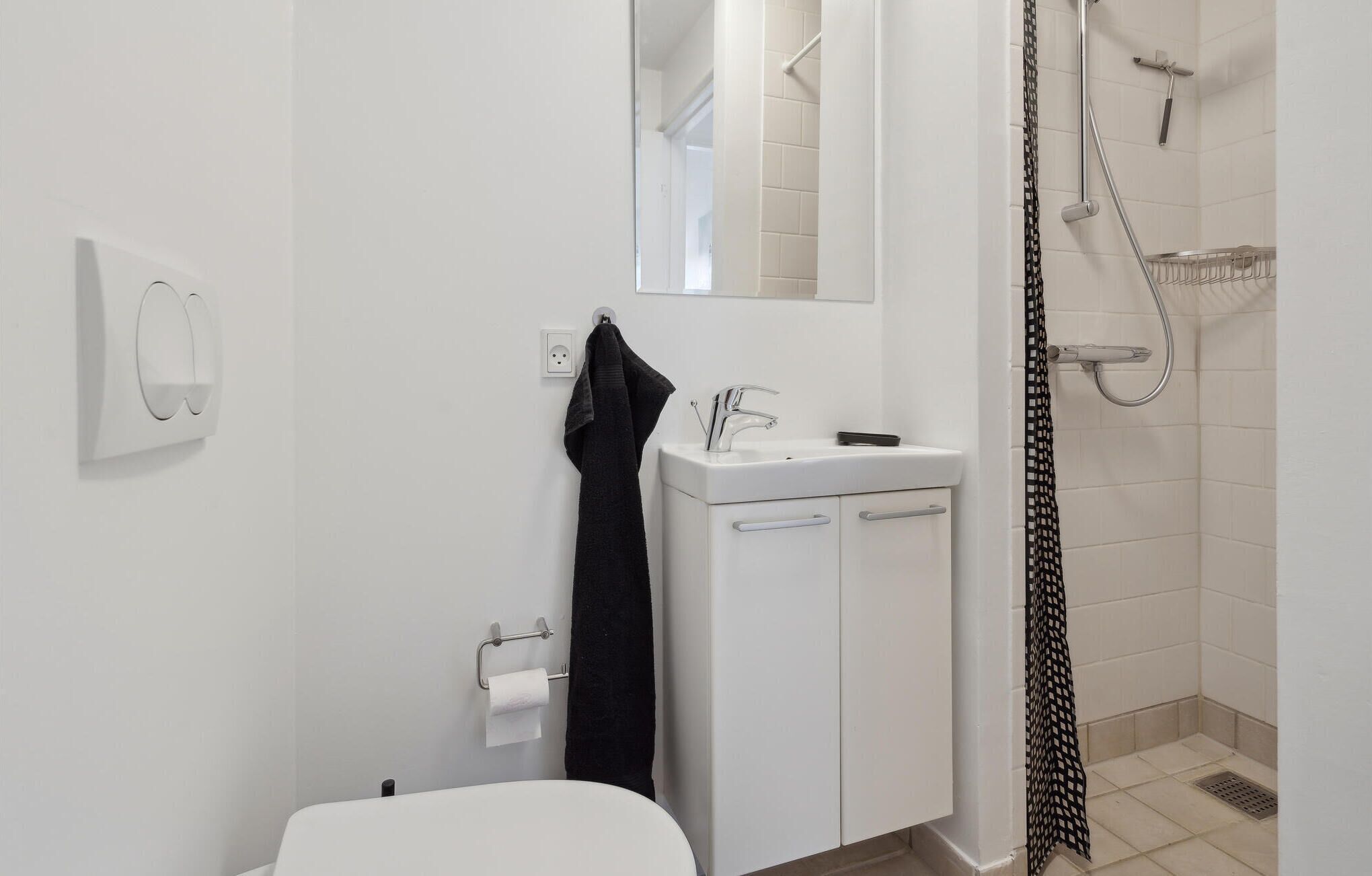 Un baño moderno con lavamanos, espejo y ducha blancos.