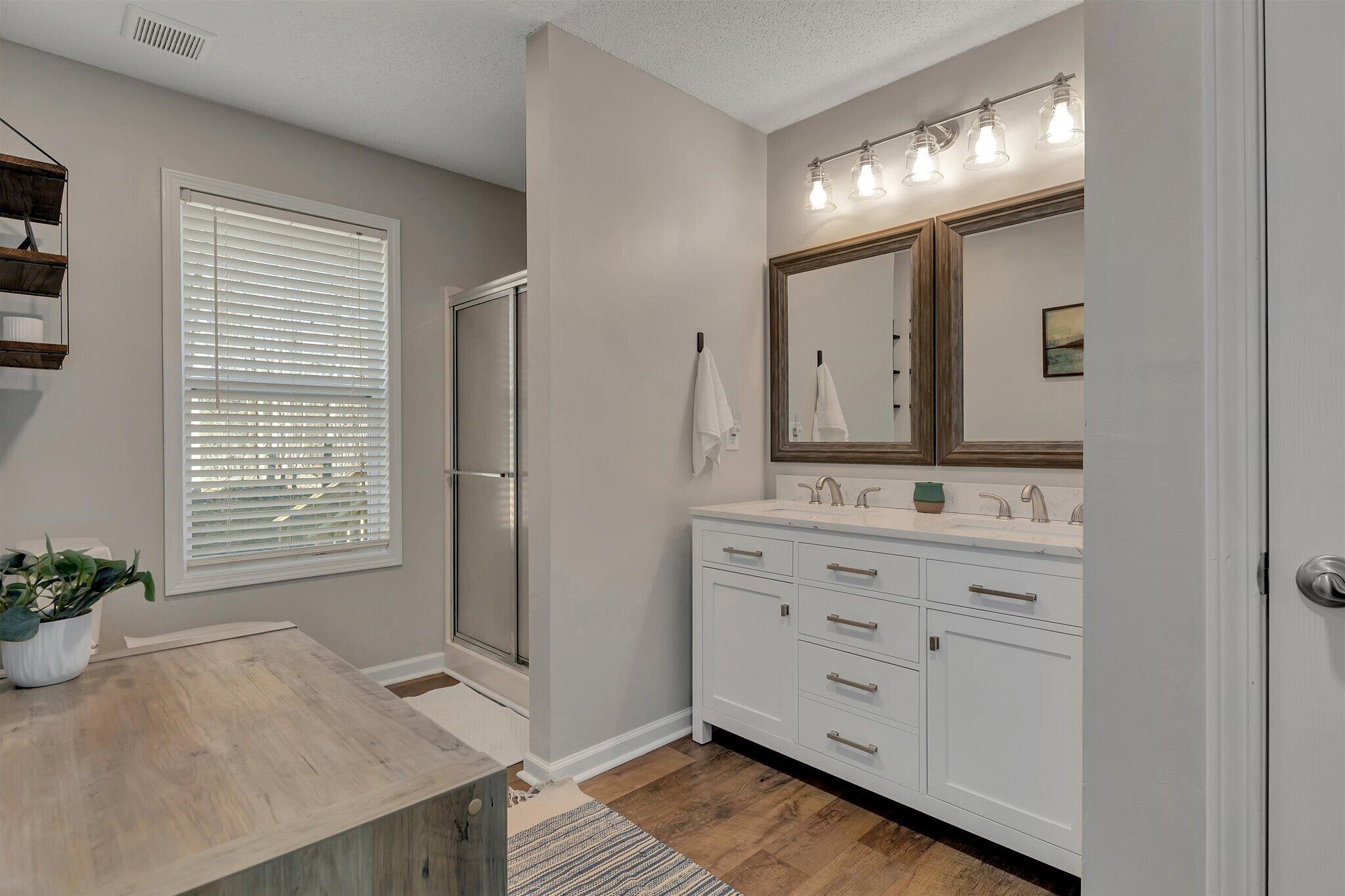 A bathroom with a shower, a sink with a mirror, and a window with blinds.