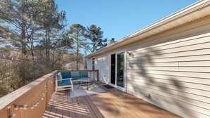 A wooden deck with a blue sofa and table, a covered patio, and a house with white siding.