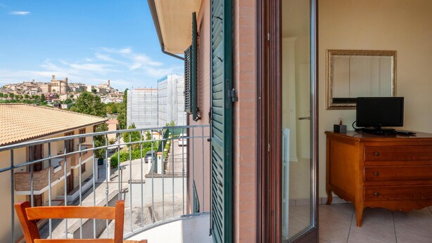 En balkon med udsigt over bybilledet, en træstol, et kommode med et fjernsyn og et spejl på væggen.