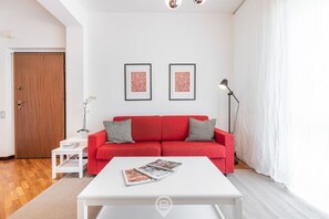 A modern living room with a red sofa, white coffee table, and two framed pictures on the wall. - Palma Paradise Escape (Cagliari)