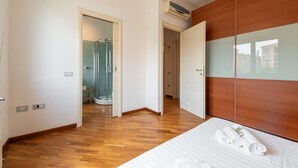 Habitació d'hotel amb sòl de fusta, llit amb roba blanca, armari de fusta i dutxa amb envà.