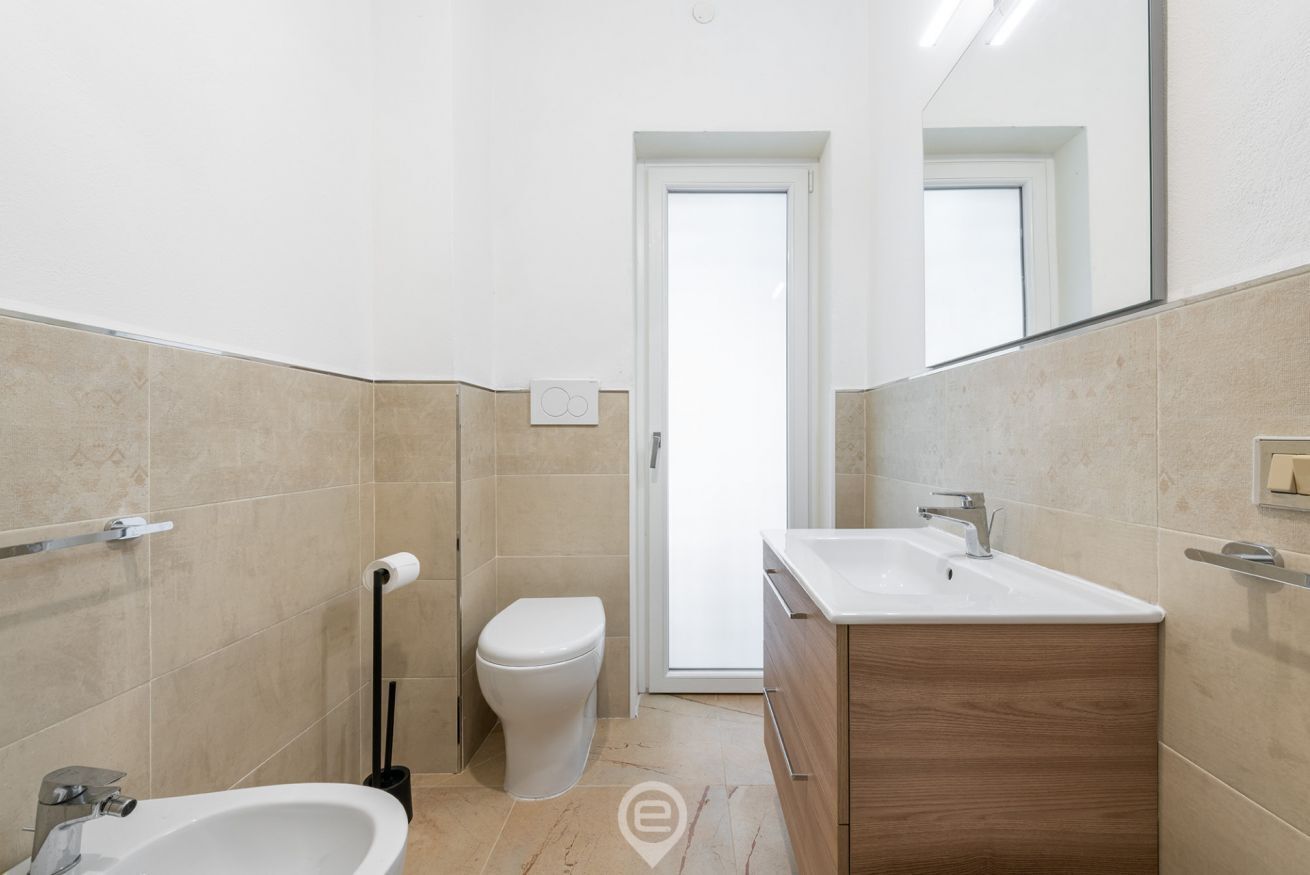 Un baño moderno con lavamanos blanco, tocador de madera y un inodoro.