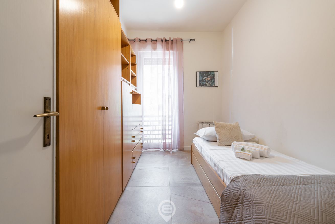 A bedroom with a bed, a wardrobe, a window with curtains, and a painting on the wall.