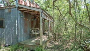 Een rustieke hut met een houten veranda en een bankje, omringd door dicht bos.