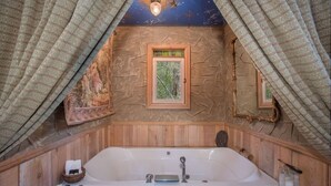 A bathroom with a large bathtub, wooden paneling, a small window, and a decorative ceiling.