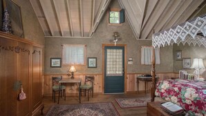 A cozy attic bedroom with a wooden ceiling, a four-poster bed, a desk with chairs, and a small window.