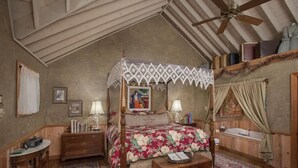 A bedroom with a four-poster bed, wooden furniture, a ceiling fan, and a bathtub.