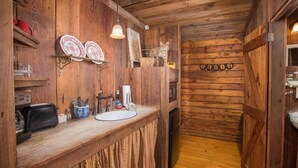 A rustic wooden interior with a wooden counter, shelves, and a refrigerator. - 7F Lodge - Batts Ferry Cabin w/Breakfast - Log Cabin w/ Jacuzzi Tub and Fire Pit (College Station)