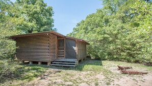 A rustic cabin with a wooden exterior and a small porch. - 7F Lodge - Batts Ferry Cabin w/Breakfast - Log Cabin w/ Jacuzzi Tub and Fire Pit (College Station)