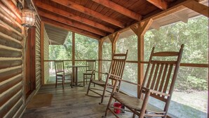 A wooden porch with rocking chairs, a table, and a lantern. - 7F Lodge - Batts Ferry Cabin w/Breakfast - Log Cabin w/ Jacuzzi Tub and Fire Pit (College Station)