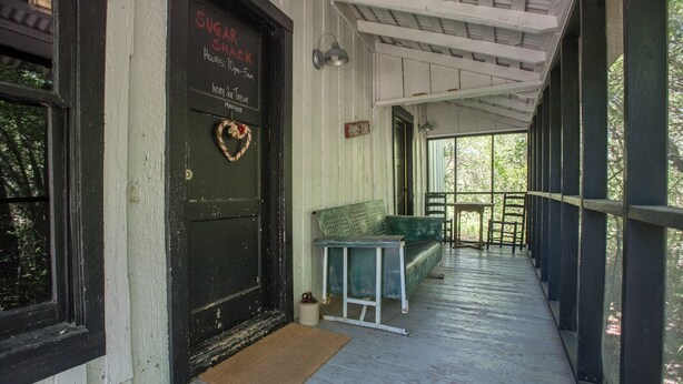 Een veranda met een zwarte deur waarop “Sugar Shack” staat en een hartvormige decoratie. Er zijn buiten zitgedeeltes met tafels en stoelen.