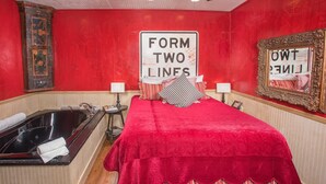 Hotelkamer met een rode wand, een groot bed met een rode sprei, een badkuip, twee bedlampen, en een bordje met de tekst 'TWEE RIJEN VORMEN'.