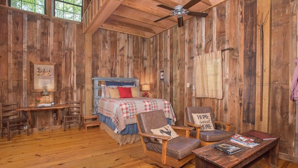 Ein rustikales Zimmer aus Holz mit einem Bett, zwei Stühlen, einem Schreibtisch und einem Deckenventilator.