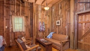 Ein rustikaler Innenraum mit Ledersofa, Holzsesseln, einem kleinen Holztisch und einer hängenden Lampe.
