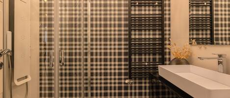 A bathroom with a checkered wall, a black and white sink, and a glass shower enclosure.
