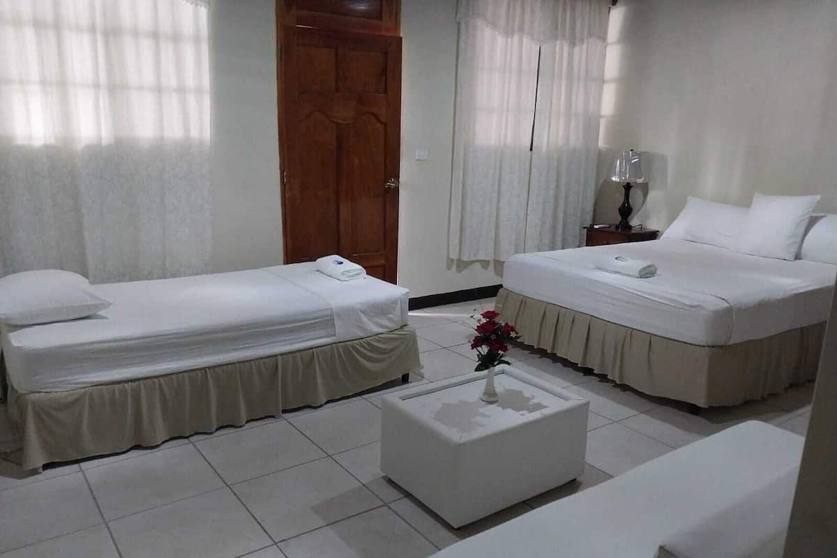 Habitación de hotel con dos camas individuales, una mesita blanca con un florero y una mesita de noche con lámpara.
