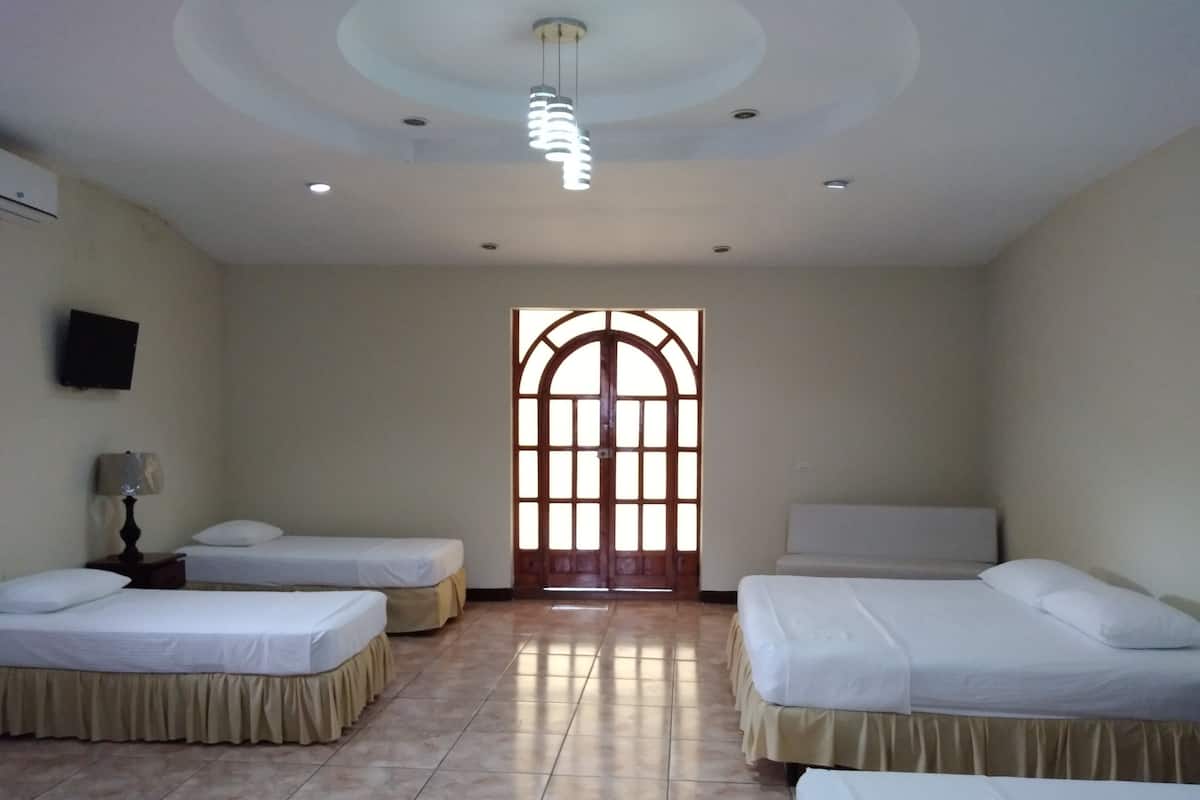Habitación de hotel con tres camas individuales, una puerta de madera con paneles de vidrio, un accesorio de iluminación en el techo y un televisor de pantalla plana en la pared.