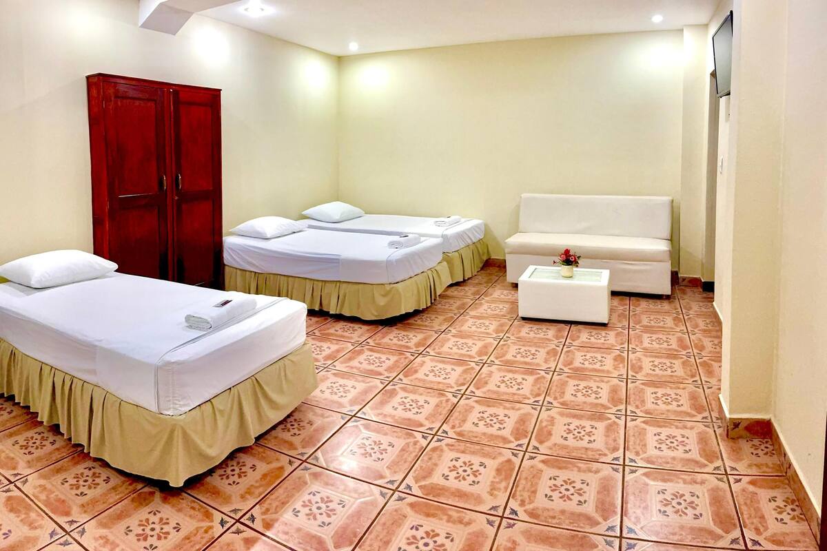 Una habitación con dos camas, un sofá, un armario rojo y una mesita con un florero.