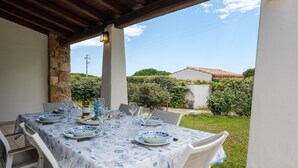 A covered outdoor dining area with a table set for four, surrounded by white chairs.