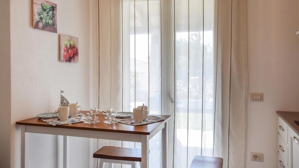 A dining area with a table set for four, a window with sheer curtains, and wall art depicting vegetables.