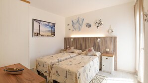 A bedroom with a wooden headboard, two beds with matching bedding, a nightstand, a wooden table with a boat, and a beach-themed painting on the wall.