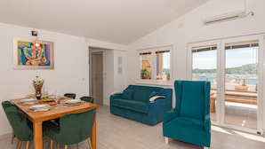 Een moderne woonkamer met een eetgedeelte, een blauwgroene fauteuil en uitzicht op een jachthaven door grote ramen.
