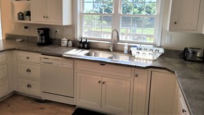 A kitchen with white cabinets, a double sink, and a window overlooking a green landscape. - Luxury Country Home, Spacious and Cozy, with Sun Room (Marionville)