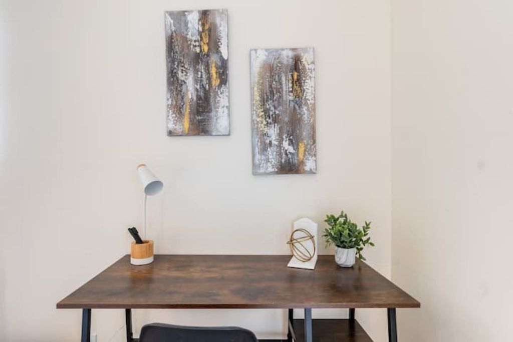 Una habitación moderna con una mesa de madera oscura, una lámpara de escritorio blanca y dos cuadros abstractos en la pared.