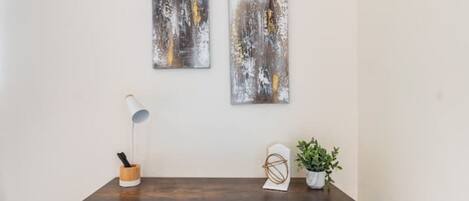 Una habitación moderna con una mesa de madera oscura, una lámpara de escritorio blanca y dos cuadros abstractos en la pared.