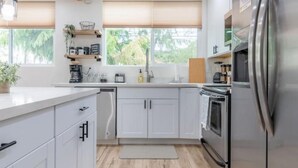 Una cocina moderna con armarios blancos, electrodomésticos de acero inoxidable y una ventana con persianas.