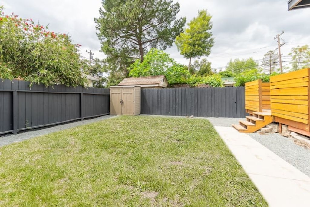 A backyard with a wooden shed, a black fence, and a yellow fence.