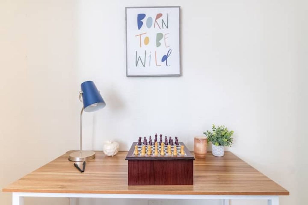 A chessboard on a wooden table with a lamp and a framed sign above.
