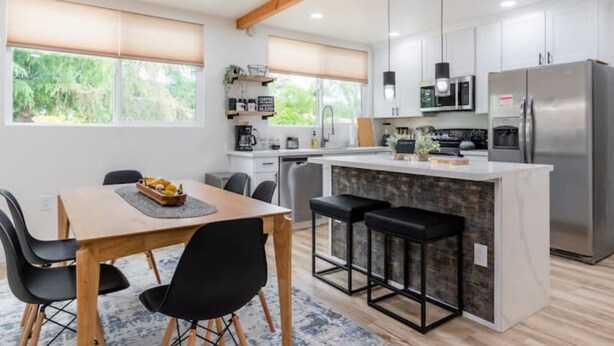 Una cocina moderna con una isla central, taburetes de bar y una zona de comedor con mesa y sillas.