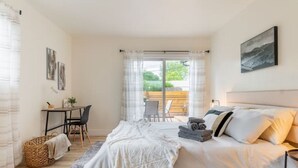 Un dormitorio con cama, escritorio y silla. Hay una ventana con cortinas, un cuadro en la pared y vistas al exterior.