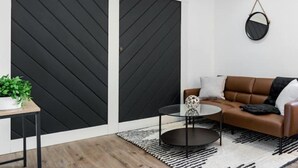 Un salon moderne avec un canapé en cuir marron, une table basse en verre et un tapis à motifs noir et blanc.
