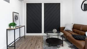 Un salon moderne avec un canapé en cuir marron, une table basse ronde, un tapis noir et un téléviseur encadré de noir.