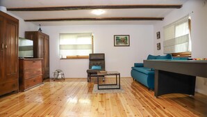 Una habitación con piso de madera, un sofá, una silla, una mesa, un ventilador y una mesa de billar.