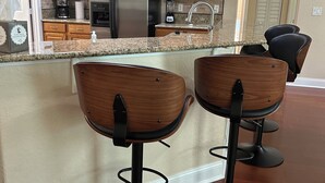 A kitchen with wooden cabinets, a stainless steel refrigerator, a coffee maker, and two bar stools. - Amazing and spacious home. 4be2Bth, and beautiful screened private pool. (Port St. Lucie)