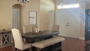 A dining area with a wooden table, cushioned chairs, and a bench. There are two doors, a chandelier, and a framed picture on the wall. - Amazing and spacious home. 4be2Bth, and beautiful screened private pool. (Port St. Lucie)