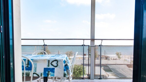 A balcony with a table and chairs, a view of the beach, and a fence.