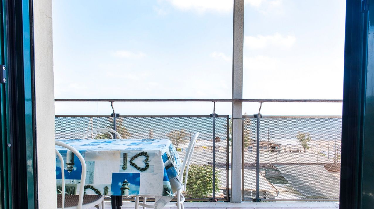 A balcony with a table and chairs, a view of the beach, and a fence.