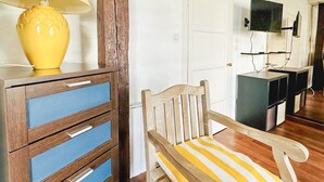 Una silla de madera con un cojín a rayas, un aparador de madera con cajones azules y una lámpara amarilla.