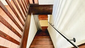 Una escalera de madera con barandilla, que conduce a un rellano con pared blanca y una puerta.