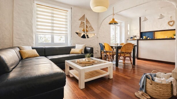 Una sala de estar moderna con un sofá de cuero negro, una mesa de centro blanca y un comedor con sillas amarillas.